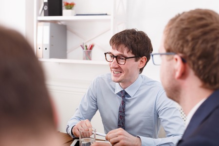 Manager team meeting. Young successful manager in glasses listen to feedbacks at office desk. White office interiorの写真素材