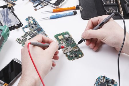 Repairing smartphone with multimeter close up. Technician pov, broken phone diagnostics at service center, repairman workplaceの写真素材