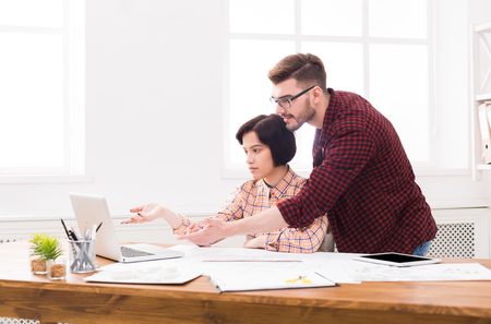 Couple of young designers working at modern office. Two coworkers discussing startup project over laptopの写真素材