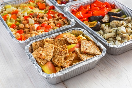 Healthy food background. Take away creative meals in foil boxes on white wood. Fitness nutrition, meat, colorful vegetable salads and fruits.の写真素材