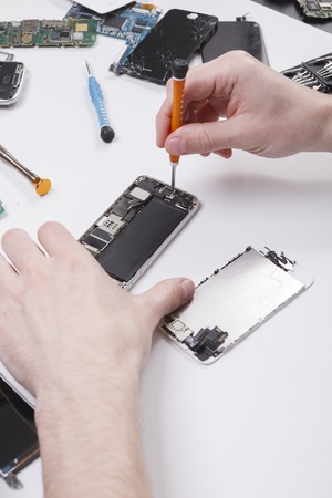 Repairman disassembling smartphone with screwdriver. Technician fixing broken phone, electronics repair service, repairer pov, copy space for textの写真素材