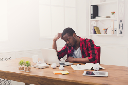 Stressed black businessman in office, in casual, work with laptop, solving a problemの写真素材