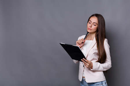 Busy elegant business woman in formal suit writing down notes to notepad, gray studio background, copy spaceの写真素材