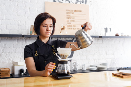 Barista preparing pourover coffee at cafe counter. Portrait of young girl in uniform at her working place. Small business, occupation people and service concept, copy spaceの写真素材