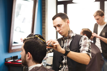 Making hipster hairstyle in male hair salon. Barbers working in barbershop with hair of clients.の写真素材
