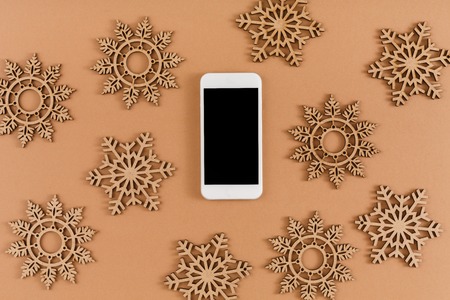 Christmas background with ornate wooden snowflakes and smartphone. New year decorations, holiday online order and shopping, seasonal sales concept, top viewの写真素材