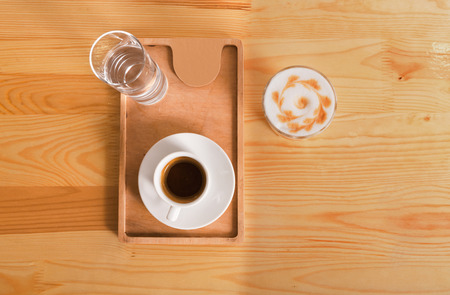 Coffee shop wooden counter background. Natural desk surface with espresso, cappuccino and glass of water on tray, top view with copy space. Coffee business concept, bar menu mockupの写真素材
