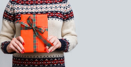 Unrecognizable woman holding christmas gift. Cropped image of girl in sweater with present box in...