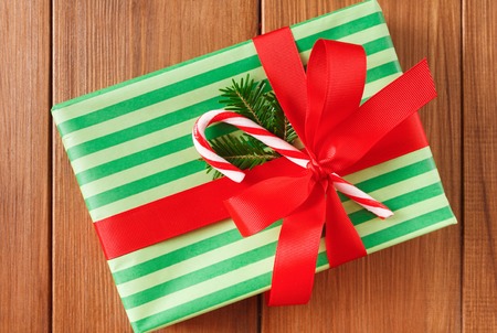 Closeup of handmade present box. Gift in striped green wrapping paper, decorated with red satin ribbon bow and candy cane lollipop, top viewの写真素材