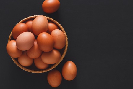Fresh brown eggs in wooden bowl on black background with copy space. Top view. Natural healthy organic food, cooking conceptの写真素材