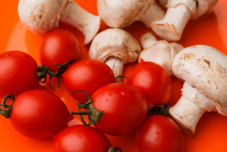 Cherry tomatoes and mushrooms on an orange background. Organic vegetables.の写真素材