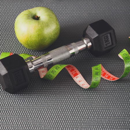 Fitness equipment. Healthy lifestyle. Dumbbells, apple and measuring tape on gray backgroundの写真素材