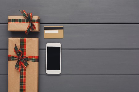 Christmas online shopping background. Craft gift boxes, mobile and credit card on gray table....