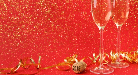 Champagne flutes and bottle cork with 2018 numbers at red holiday background with golden glitters and tinsel. Celebrating christmas, new year or birthday. Mockup for xmas postcard, cropの写真素材