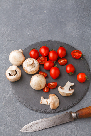 Cut tomatoes and mushrooms on rustic slate stone plate. Cooking healthy food on gray background, copy space.の写真素材