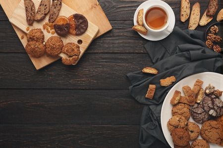 Sweet winter holidays background with various cookies and cup of hot spicy black tea on dark rustic table with copy space. Cooking christmas biscuits and biscotti, top view. Mockup for recipeの写真素材