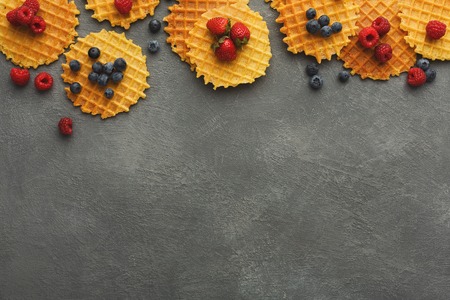 Belgium waffles with berries on gray background. Border of checkered cookies top view with copy space. Sweet food and tasty breakfast conceptの写真素材