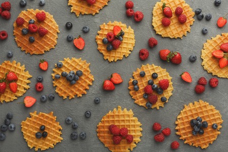Traditional belgian waffles with fresh berries on gray background. Flat lay, top view on sweet crispy snack. Sweet breakfast and bakery shop conceptの写真素材