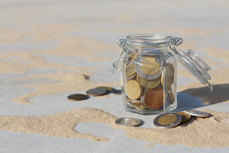 Coins in glass jar on gray floor with sand background, copy space. Money box, saving money for dream, pension, vacation. Financial stability conceptの写真素材