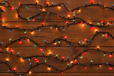 Christmas lights on wood background. Holiday shiny garland top view. Xmas tree decorations, winter...