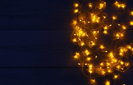 Christmas lights background, copy space. Holiday shiny garland border top view on wooden planks surface. Xmas tree decorations, winter holidays illuminationの写真素材