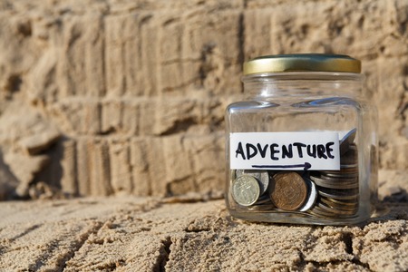 Glass jar with coins for adventure on rock background, copy space. Money box, distribution of cash savings concept.の写真素材