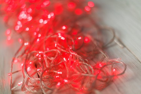 Christmas red lights background. Holiday shiny garland on light wooden planks surface. Xmas tree decorations, winter holidays illuminationの写真素材
