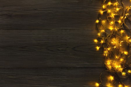 Christmas lights background, copy space. Holiday shiny garland border top view on dark grey wooden planks surface. Xmas tree decorations, winter holidays illuminationの写真素材