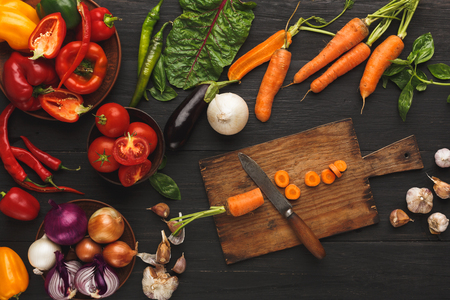 Cooking ingredients background. Sliced carrots and vintage knife on cutting board, vegetables, herbs and spices on kitchen table. Vegetarian cuisine and food preparation concept, top viewの写真素材