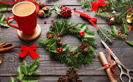 Creative leisure background. Christmas diy hobby in cozy atmosphere with hot coffee cup. Handmade craft xmas wreath, tools, trinkets and scissors on rustic wooden tableの写真素材