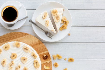 Delicious banana cake with coffee cup on table top view. Sliced fruit biscuit with caramel and buttercream on wooden catering plate, copy spaceの写真素材