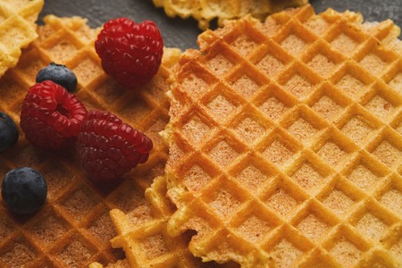 Belgium waffles with berries background. Closeup of checkered texture, fresh raspberries and blueberries on top. Sweet food and tasty breakfast concept.の写真素材