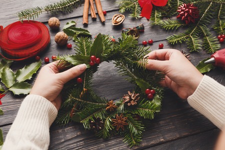 Point of view of wooden table background with female hands making wreath. Creative leisure, cup, tools and trinkets for xmas holiday decoration.の写真素材