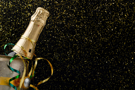 Celebrating new year, birthday, xmas party. Bottle of champagne in a bucket and colorful tinsel on black backgroud with golden glitters, copy space. Mockup for postcardの写真素材