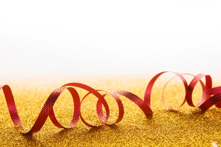 Curly red serpentine on golden glitter on white background, copy space. Christmas and new year holiday concept. Bright luxury celebration backdropの写真素材