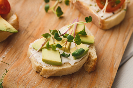 Healthy sandwiches with creamy cheese, avocado, cucumber, cherry tomatoes and micro greens on rustic wooden board. Vegetarian snackの写真素材