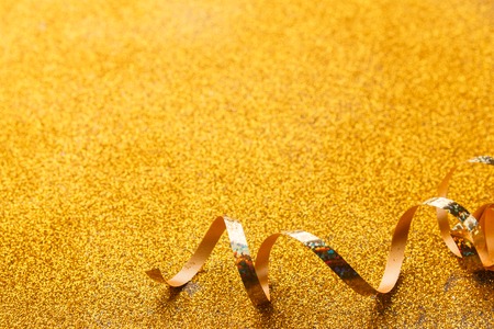 Curly golden serpentine on shiny glitter background, top view, copy space. Christmas and new year holiday concept. Bright luxury celebration backdropの写真素材