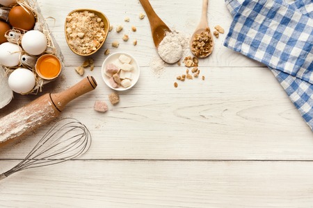 Cooking ingredients background. Border of flour, eggs, raisins, sugar and kitchen utensils on white rustic wood with copy space. Dough preparing and pastry concept, top viewの写真素材