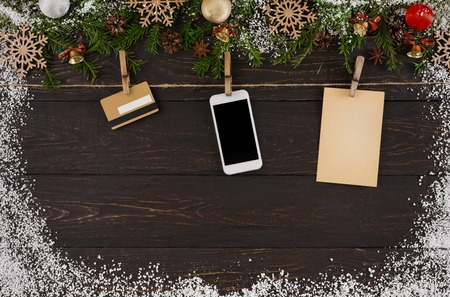 Christmas background, twine rope with cell phone, credit card and paper sheet. Garland frame, top view with copy space on rustic wooden table surface sprinkled with snow. Winter holidays celebration.の写真素材