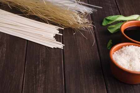 Different kinds of pasta on wooden table. Homemade soba, rice noodles, spaghetti with rice, soy sauce and spinach, copy spaceの写真素材