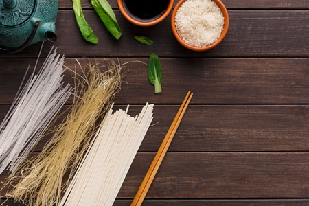 Different kinds of pasta on wooden table. Homemade soba, rice noodles, spaghetti with rice, soy sauce, spinach and chopsticks, copy spaceの写真素材