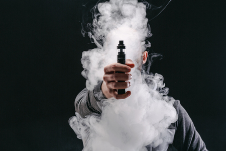 Unrecognizable man in the cloud of vape smoke. Guy smoking e-cigarette to quit tobacco. Vapor and alternative nicotine free smoking concept, copy spaceの写真素材