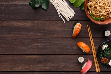 Bowl of rice noodles with soy sauce and chopsticks on wooden background, with pasta variety, spinach...