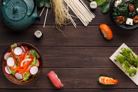Bowl of miso soup with tofu cheese, salad with onion, pepper and radish, with pasta variety, pot and sushi on wooden background, copy space, top viewの写真素材