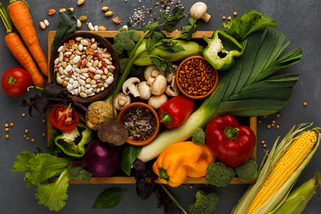 Heap of fresh organic vegetables and greens on wooden tray at black wood background. Healthy natural food. Carrots, pepper, beans and other cooking ingredients top viewの写真素材
