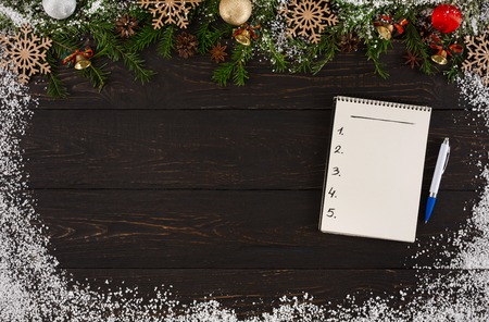Blank notepad for wish list or letter to Santa at dark wooden table background decorated with snow and fir tree twigs garland, top view with copy space. Preparing for winter holidays conceptの写真素材