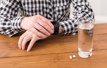 Taking pills. Unrecognizable senior man hands on table with glass of water and medicine. Healthcare, treatment, aging concept, copy spaceの写真素材