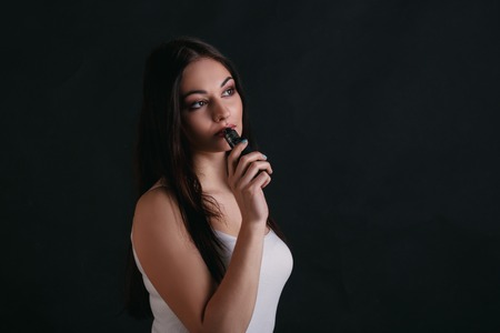 Girl with vaping at black studio background. Young woman smoking e-cigarette to quit tobacco. Vapor...