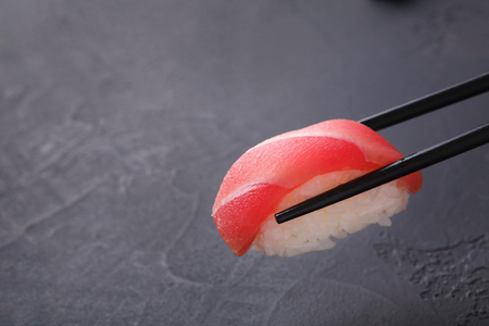 Eating sushi at restaurant. Chopstick taking one nigiri sushi with tuna on black background, japanese cuisine, copy spaceの写真素材