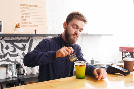 Handsome bearded barman preparing tasty coffee non-alcoholic cocktail with orange juice and mint...